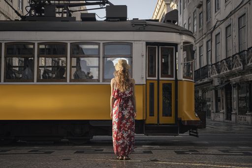 A young female tourist standing in front of a passing tramway surrounded by buildings at daytime