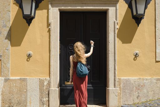 A young female in a red dress knocking on the door under the sunlight at daytime