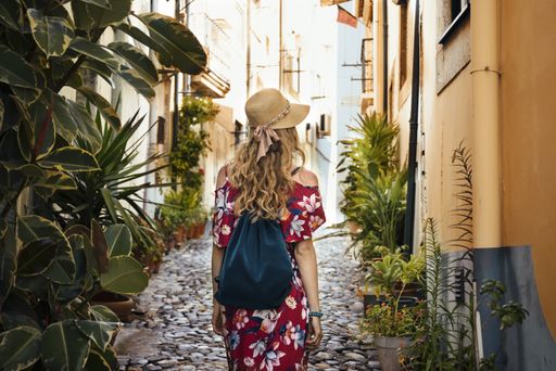 A young female tourist in a red floral dress walking through an alley surrounded by buildings at daytime