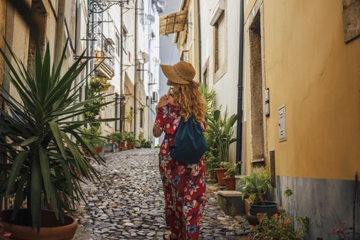 A young female tourist in a red floral dress walking through an alley surrounded by buildings at daytime