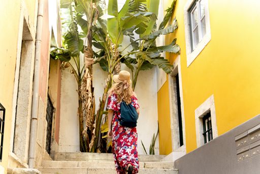 A young female tourist climbing up the stairs of a yellow building under the sunlight