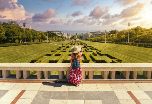 A young female tourist in a red floral dress in The Eduardo VII Park under the sunlight in Portugal