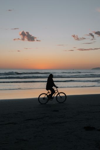 A man riding bicycle on the beach during scenic sunset