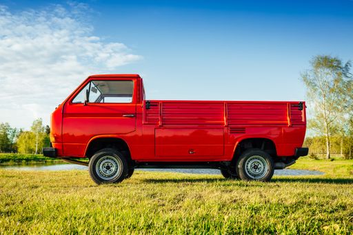 A closeup shot of a red truck on the green field next to the water