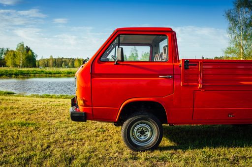A closeup shot of a red truck on the green field next to the water