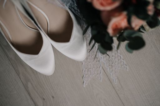 A top view of flowers with bride white shoes on ground