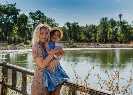 A blonde mom hugging her little daughter next to the lake reflecting the trees