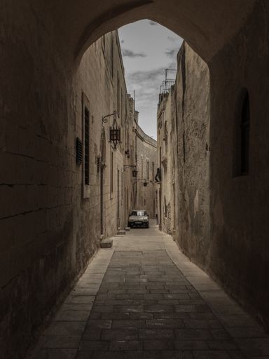 A vertical shot of a car parked on a narrow pathway in the middle of buildings