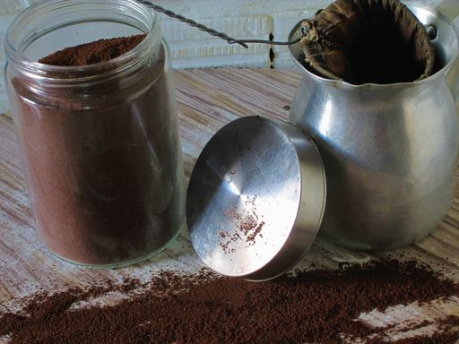 A closeup shot of a glass jar filled with coffee powder and an aluminum jug with a cloth strainer
