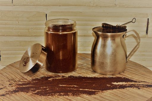 A closeup shot of a glass jar filled with coffee powder and an aluminum jug with a cloth strainer