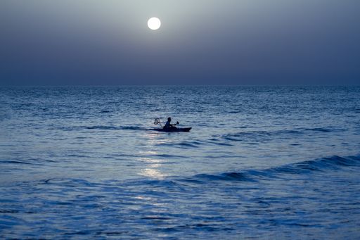 A fisherman fishing in the wavy  ocean at night under the gleaming full moon