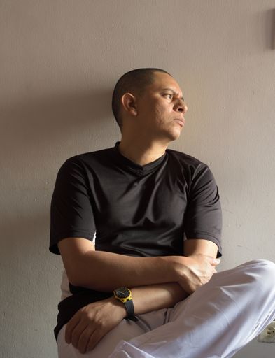 A vertical closeup shot of a Latin male with thoughtful expression sitting leaned on the wall