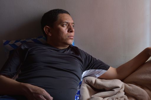 A middle-aged Hispanic male lying on the bed with a concerned face expression