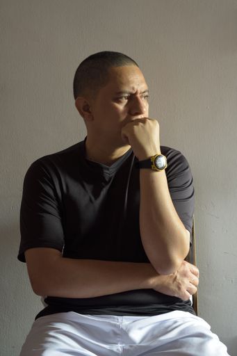 A vertical portrait of a Hispanic male sitting with a worried face expression