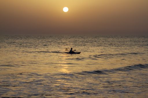 A fisherman fishing in the wavy ocean under the gleaming yellow sunset