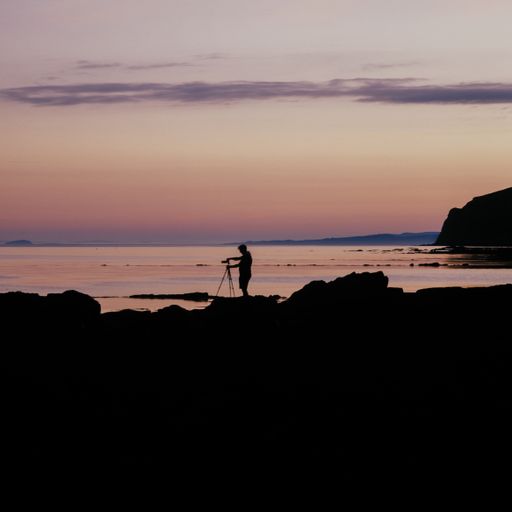 A silhouette shot of a person on the beach filming the beautiful colors of the sunset