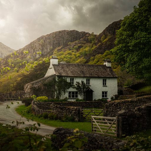 A beautiful white cottage in the middle of tall hills and green nature against a cloudy dark sky