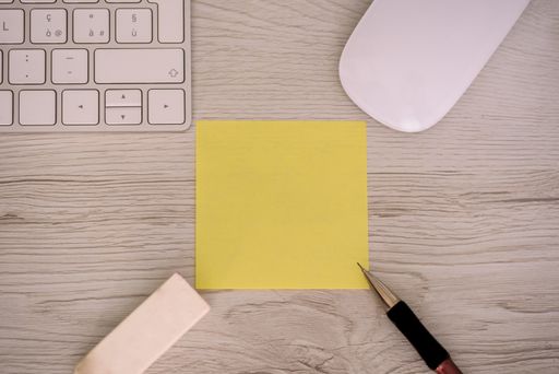 An overhead top view of a keyboard, mouse, pencil, and eraser around a notepad on a wooden background