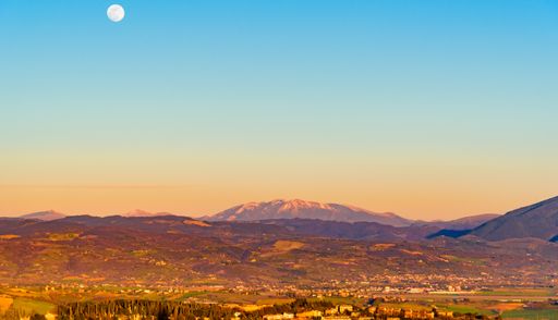 A panoramic shot of a beautiful landscape under a blue sky with a full moon