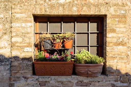 A brick building window decorated with beautiful colorful flowers in ancient pots