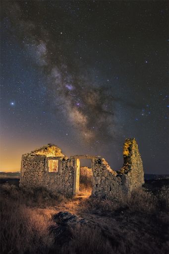 A vertical shot of an old abandoned broken ancient building in the background of a starry sky.