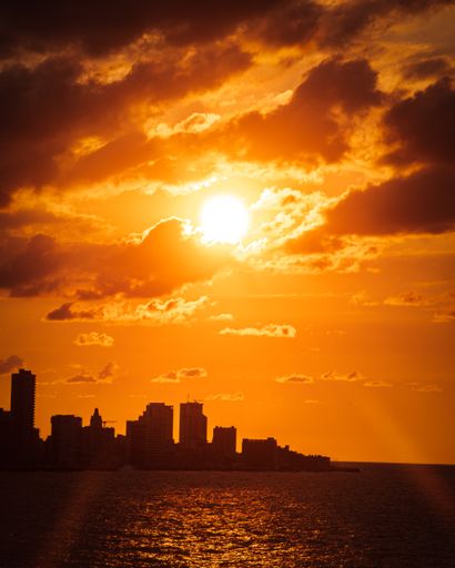 A vertical shot of the silhouettes of buildings and a sea under the light of the golden sun at sunset
