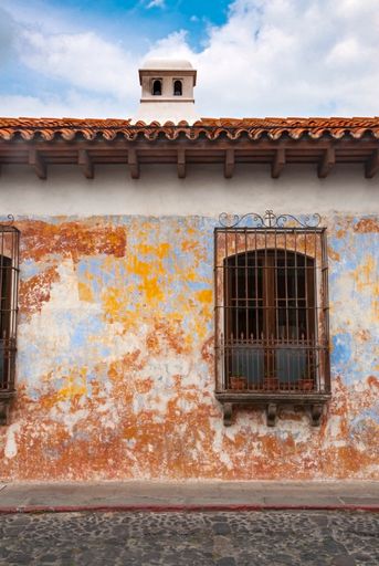 Colonial style house facade in the city of La Antigua Guatemala, with fireplace and wrought iron balconies, cobblestone street and blue sky, natural l