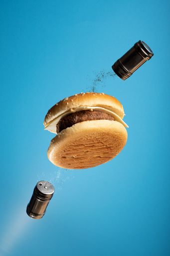 A dynamic food poster with flying hamburger and salt and pepper shaker against blue background