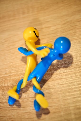 A vertical closeup of two yellow and blue small toys with smiling faces on the wooden table