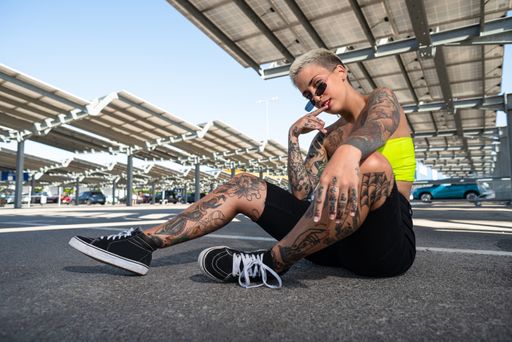 A pretty caucasian woman with tattooed body and sunglasses in a commercial car park