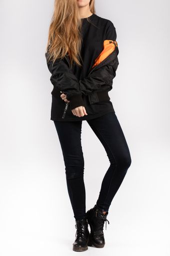 A young female wearing a black jacket standing against a white wall