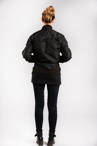 A young female wearing a black jacket standing against a white wall