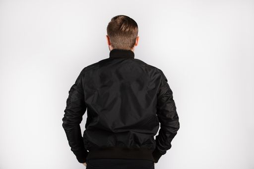 A young male wearing a black jacket standing against a white wall