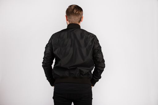 A young male wearing a black jacket standing against a white wall