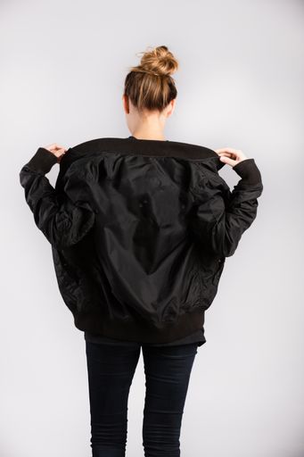 A young female wearing a black jacket standing against a white wall