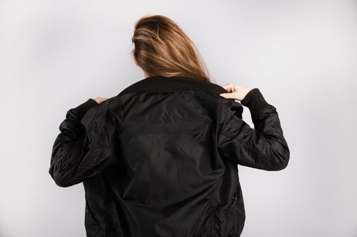 A young female wearing a black jacket standing against a white wall