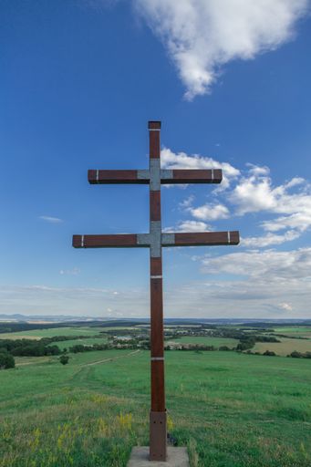 A vertical shot of a cross statue in a landscape under the cloudy skies