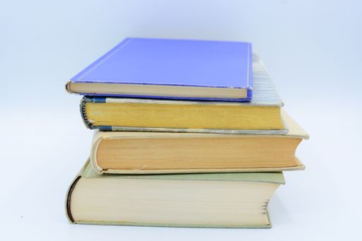 A closeup shot of four books stacked over one another on a white background