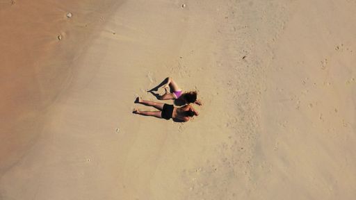 An aerial shot of a Caucasian couple laying and tanning on the beach of Gili Meno, Lombok, Indonesia