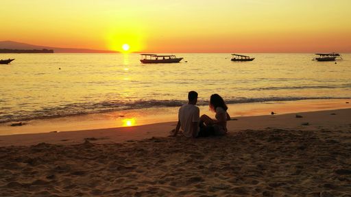 A couple watching out into the horizon at the sun setting on the beach of Gili Meno, Lombok, Indonesia
