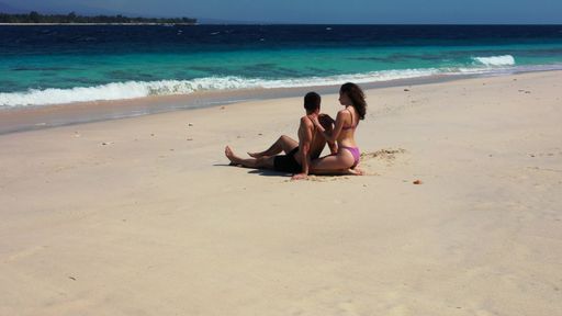 A Caucasian woman applying sunscreen on her boyfriend sitting on the beach in Gili Meno, Indonesia