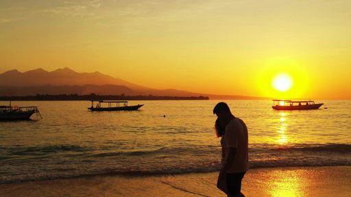 A silhouette shot a Caucasian couple walking on the beach at sunset in Gili Meno, Lombok, Indonesia