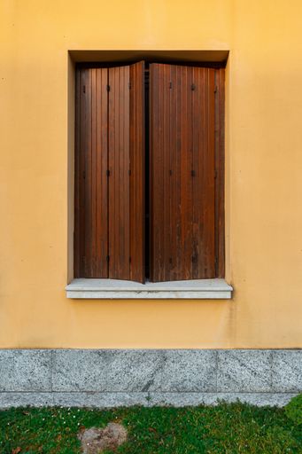 A vertical shot of a brown wooden window cover on a yellow wall