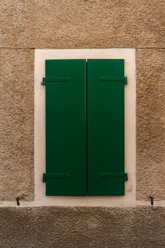 A vertical shot of a green wooden window cover on a yellow wall