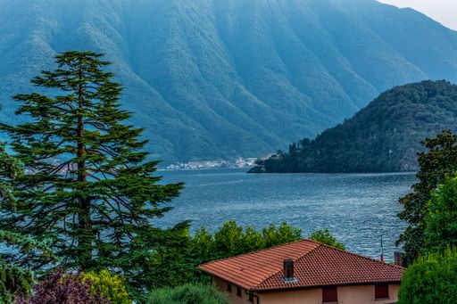 A beautiful scene of  trees, houses in Lake Como, Italy with mountains and blue sky in the background