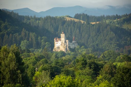 A scenic view of Bran Castle surrounded by forests with mountains in the background