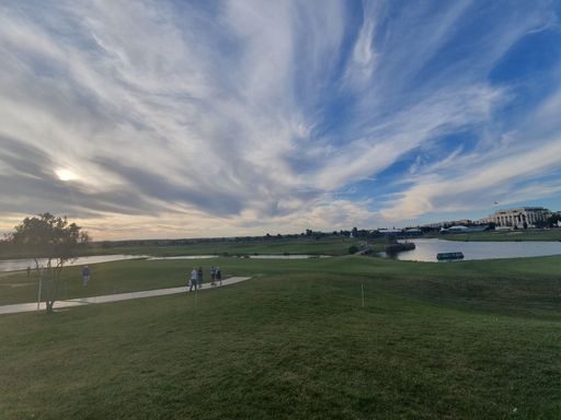 A beautiful shot of a golf field next to ponds in the cloudy sky.