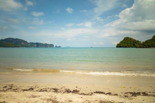 A wide shot of green islets on the body of the sea with sandy shore under a blue sky
