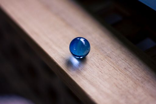 A closeup shot of a shiny blue marble on a wooden surface