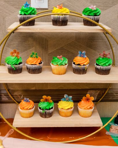 A view of cupcakes in different flavors topped with colorful cream and edible flowers on shelves on the table